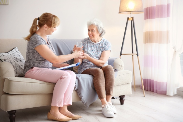 A home caregiver helps an elderly client with household tasks like getting water.