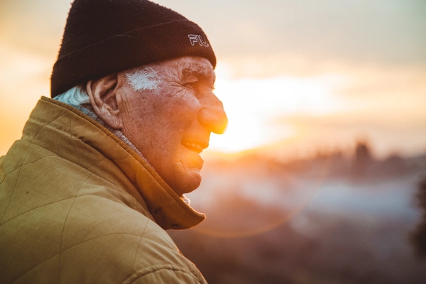 An elderly man stares off camera while the sun comes up in the background.